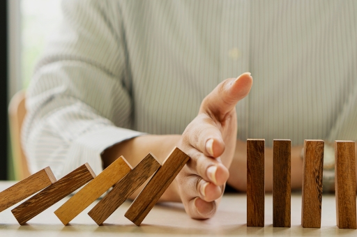 Ein Mann verhindert mit seiner Hand, dass Dominosteine umfallen