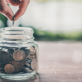Eine Person gibt eine Münze in ein Glas mit Münzen