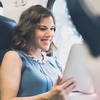 Eine Frau sitzt im Zug und sieht sich ihr Tablet an