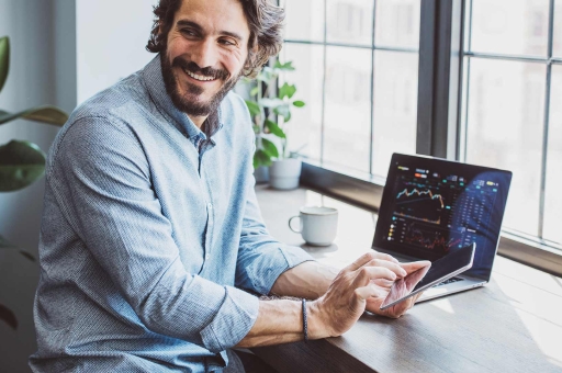 Ein Mann sitzt vor seinem Notebook und tippt auf sein Smartphone