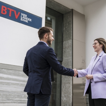 Ein Mann und eine Frau geben sich stehend die Hand.